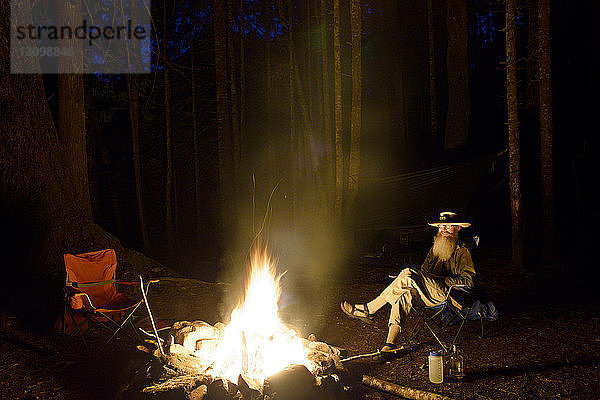 Mann entspannt sich nachts am Lagerfeuer im Wald