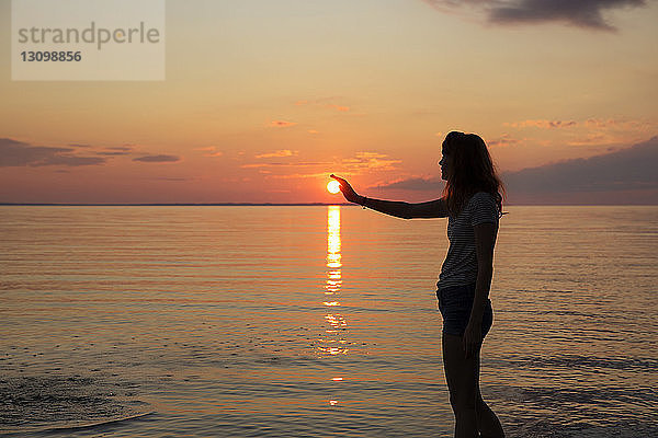 Silhouette eines Teenager-Mädchens  das die Sonne berührt  während es am Strand steht