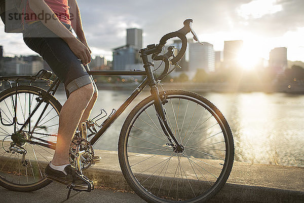 Niedriger Abschnitt eines Mannes  der bei Sonnenuntergang auf der Straße am See Fahrrad fährt