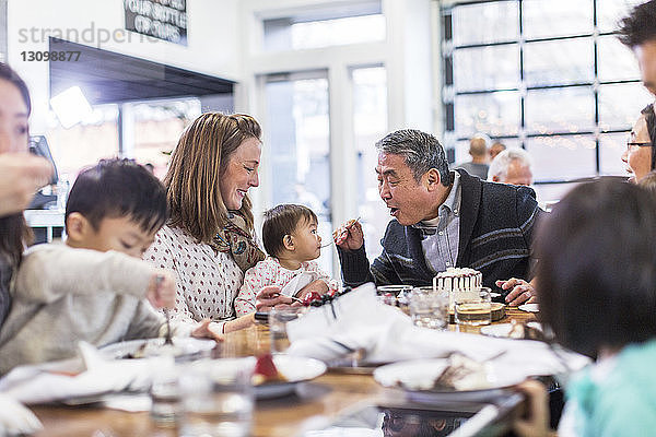 Großvater füttert ein kleines Mädchen mit Kuchen  während er mit der Familie im Restaurant sitzt
