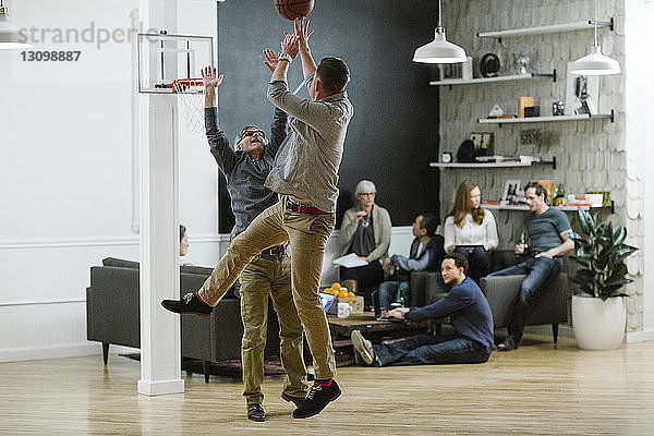 Geschäftsleute spielen Basketball  während ihre Kollegen im Hintergrund im Büro sitzen