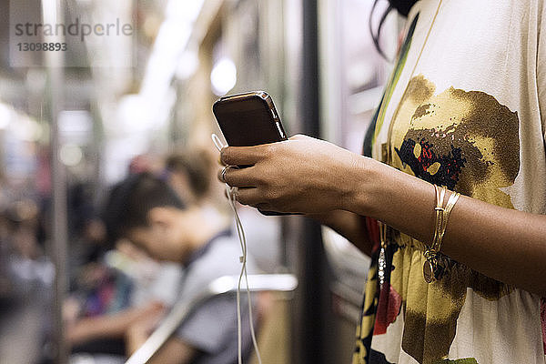 Mittelsektion einer Frau  die Mobiltelefon und Kopfhörer im Zug hält