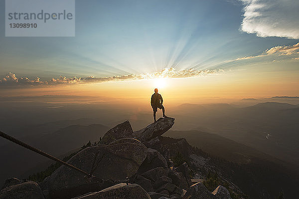 Mann steht bei Sonnenuntergang auf Fels an Klippe gegen Himmel