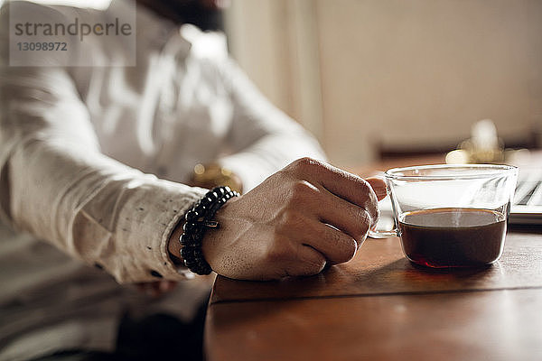 Ein Mann hält eine schwarze Kaffeetasse am Tisch