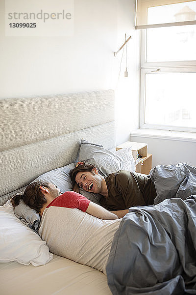 Fröhliches homosexuelles Paar entspannt zu Hause im Bett
