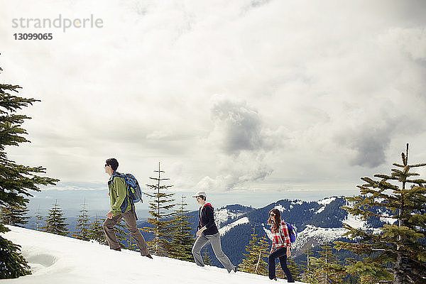 Freunde wandern auf schneebedecktem Berg vor Wolken