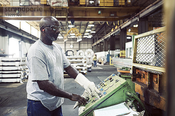 Seitenansicht eines Arbeiters bei der Arbeit in der Stahlindustrie  der eine Kontrollmaschine benutzt