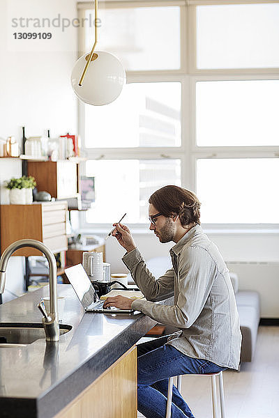 Seitenansicht eines Mannes mit Laptop-Computer auf der Kücheninsel zu Hause