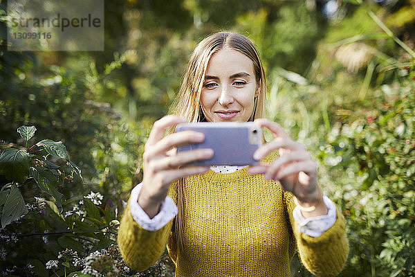 Junge Frau fotografiert im Stehen inmitten von Pflanzen