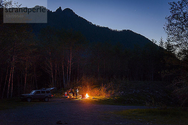 Wanderer zelten in der Dämmerung am Lagerfeuer gegen die Berge