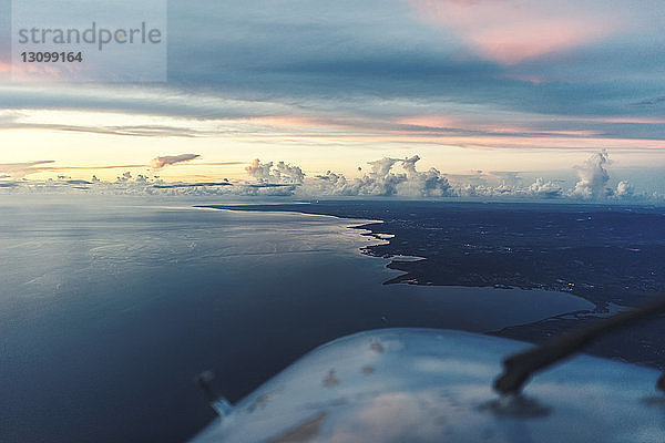 Ausschnitt eines Flugzeugs  das bei Sonnenuntergang über die Seelandschaft gegen einen bewölkten Himmel fliegt