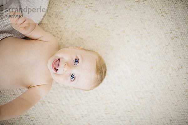 Draufsicht auf Baby  das lachend zu Hause auf dem Teppich liegt