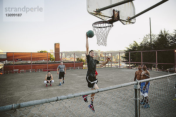 Freunde beobachten  wie ein Mann beim Üben von Basketball vor Gericht eintaucht