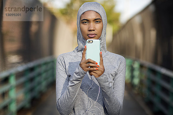 Porträt einer Frau mit Kapuzenhemd bei der Benutzung eines Smartphones auf einem Fußweg