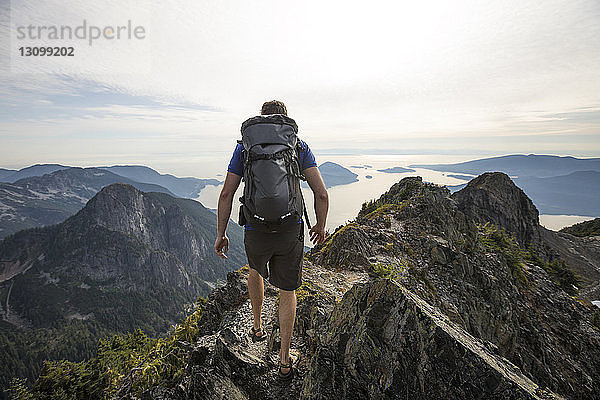 Rückansicht eines Wanderers mit Rucksack beim Wandern auf Berg gegen Himmel