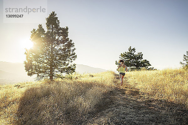 Rückansicht einer Frau  die an einem sonnigen Tag auf einem Berg vor klarem Himmel joggt
