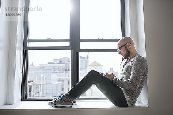 Seitenansicht eines Mannes  der ein Smartphone benutzt  während er am Fenster sitzt