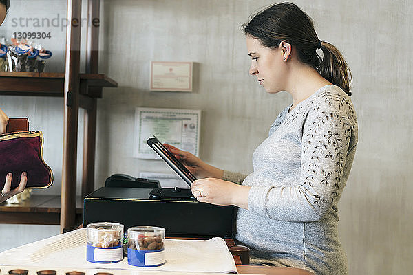 Seitenansicht einer schwangeren Besitzerin  die einen Tablet-Computer am Ladentisch benutzt