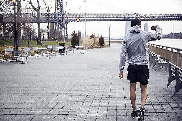 Rückansicht eines männlichen Sportlers  der die Williamsburg-Brücke beim Gehen auf einem Fußweg fotografiert