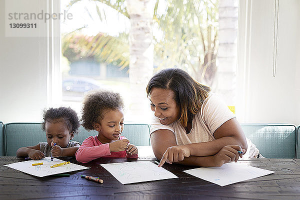 Fröhliche Mutter zeigt auf Papier mit Töchtern gegen Fenster zu Hause