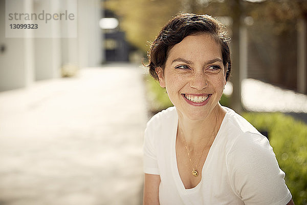 Nahaufnahme einer glücklichen Frau  die beim Sitzen im Freien wegschaut