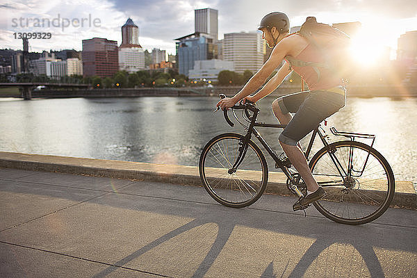 Mann trägt Rucksack  während er bei Sonnenuntergang auf der Straße Fahrrad fährt
