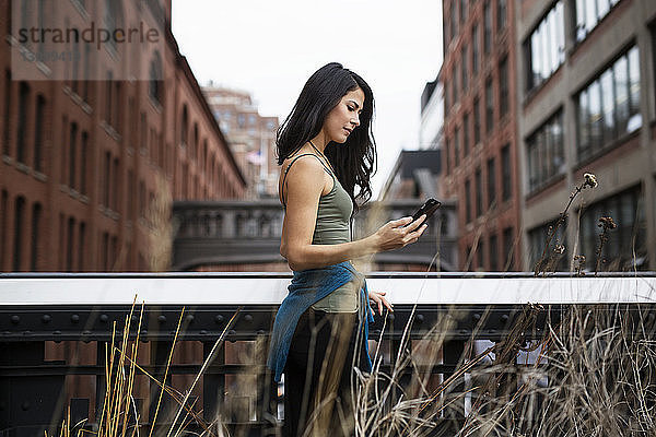 Seitenansicht einer Frau mit einem Smartphone auf der Brücke mit der Staple Street Skybridge im Hintergrund