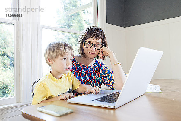 Mutter sieht ihren Sohn zu Hause am Laptop auf dem Tisch an