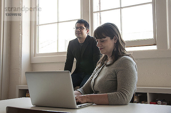 Geschäftsfrau benutzt Laptop-Computer  während ein Geschäftsmann im Hintergrund in einem neuen Büro sitzt
