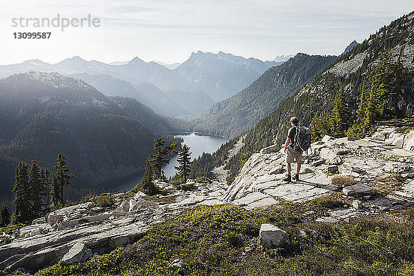 Rückansicht eines Mannes  der auf einer Klippe vor einer Bergkette steht