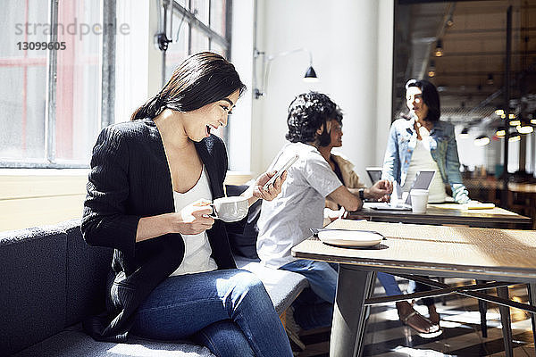 Glückliche Geschäftsfrau nutzt Smartphone mit Geschäftsleuten  die im Hintergrund arbeiten