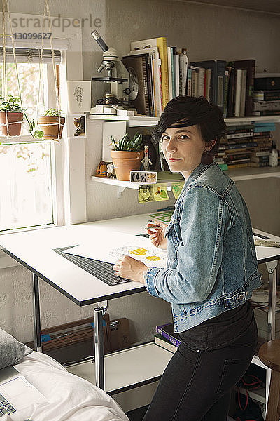 Porträt einer Künstlerin  die einen Stift hält und an einem Tisch steht
