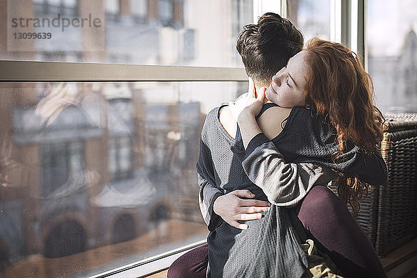 Lesbisches Paar umarmt sich  während es zu Hause auf dem Fensterbrett sitzt