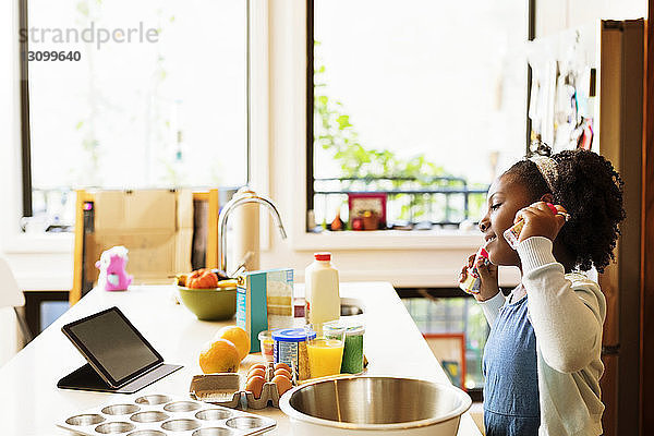 Mädchen sieht Rezept im Tablet-Computer  während sie in der Küche Cupcakes backt