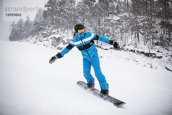 Mann beim Snowboarden an Bäumen auf schneebedecktem Berg