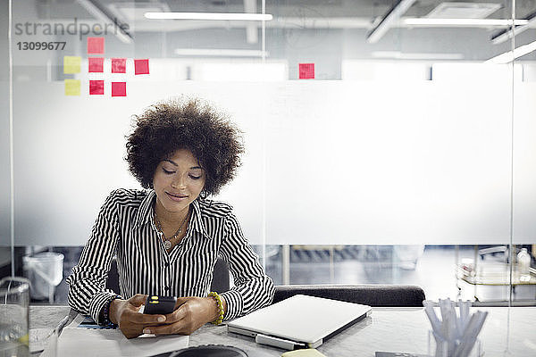 Geschäftsfrau benutzt Smartphone  während sie im Büro sitzt