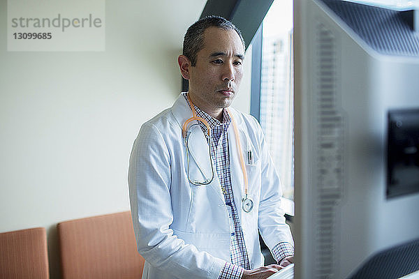 Zuversichtlicher männlicher Arzt mit Desktop-Computer auf der Krankenhausstation