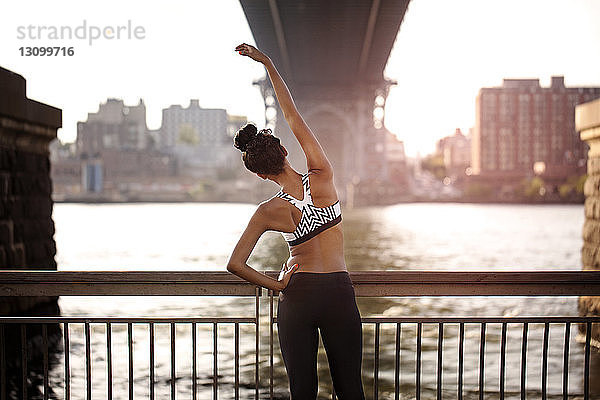Rückansicht einer sportlichen Frau  die sich am Geländer unter der Williamsburg Bridge streckt