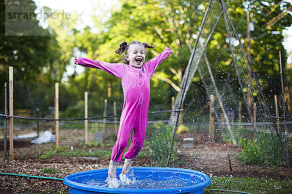 Fröhliches Mädchen springt im Planschbecken auf dem Feld