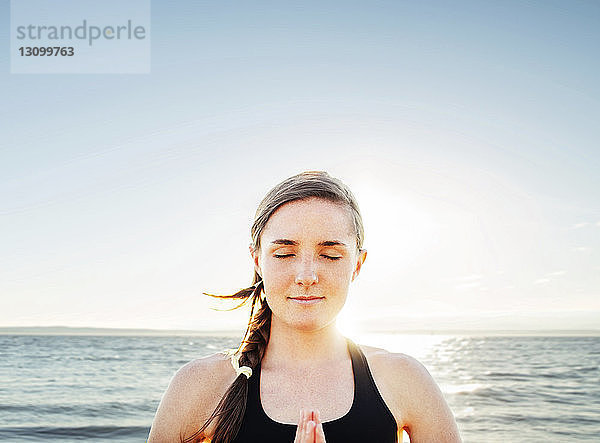 Frau meditiert in Lotus-Position am Meer gegen den Himmel