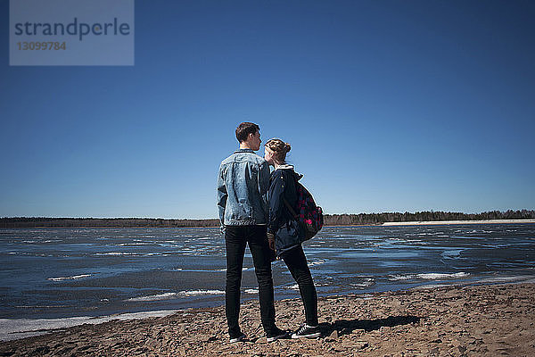 Paar steht am Strand vor klarem  blauem Himmel am sonnigen Tag