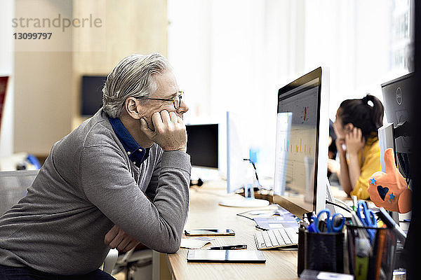 Geschäftsmann schaut auf Desktop-Computer mit einer Kollegin im Hintergrund
