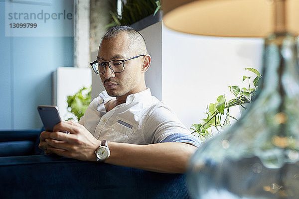 Geschäftsmann benutzt Mobiltelefon  während er im Kreativbüro auf dem Sofa sitzt