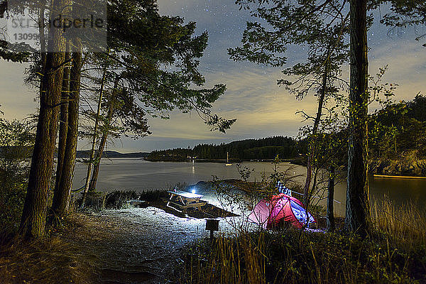 Beleuchtetes Zelt am See im Wald in der Dämmerung