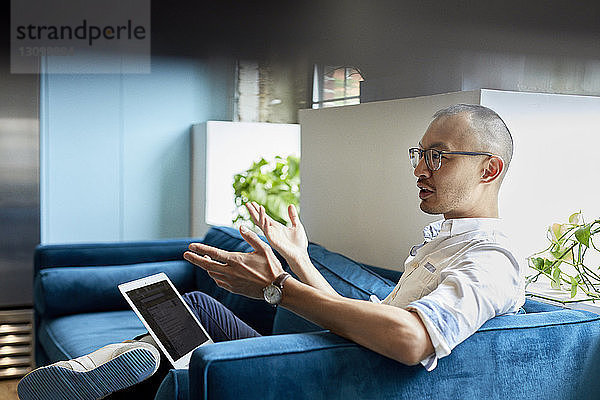 Geschäftsmann mit Laptop gestikuliert  während er im Kreativbüro auf dem Sofa sitzt