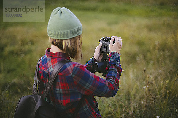 Seitenansicht einer Frau mit Rucksack beim Fotografieren im Stehen auf einem Grasfeld