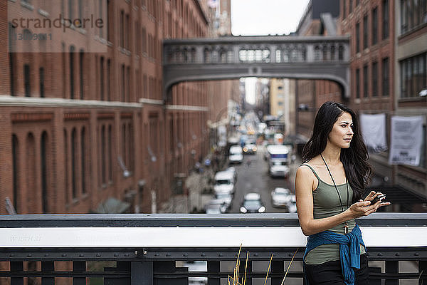 Nachdenkliche Frau hält Smartphone auf der Brücke mit der Staple Street Skybridge im Hintergrund