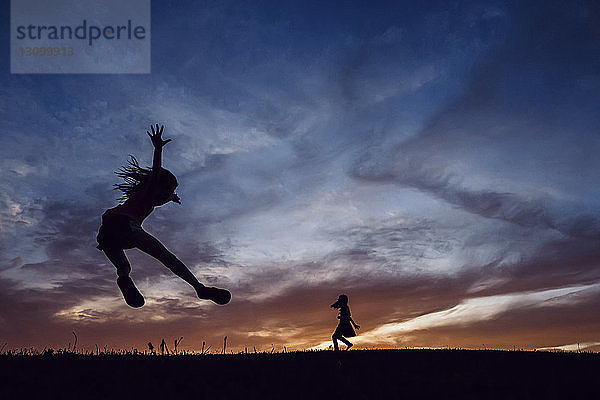 Scherenschnittschwestern spielen auf dem Spielfeld gegen den dramatischen Himmel bei Sonnenuntergang