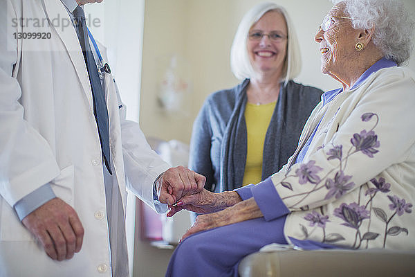 Männlicher Arzt hält Hand und spricht mit weiblicher Patientin  die neben der Tochter auf der Krankenhausstation sitzt
