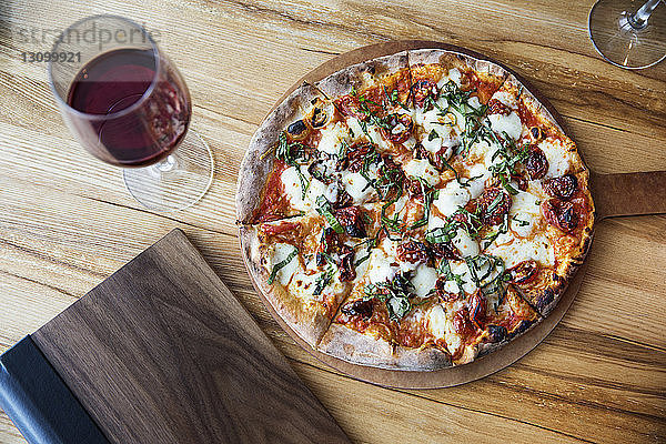 Draufsicht auf frische Pizza mit rotem Weinglas auf dem Restauranttisch